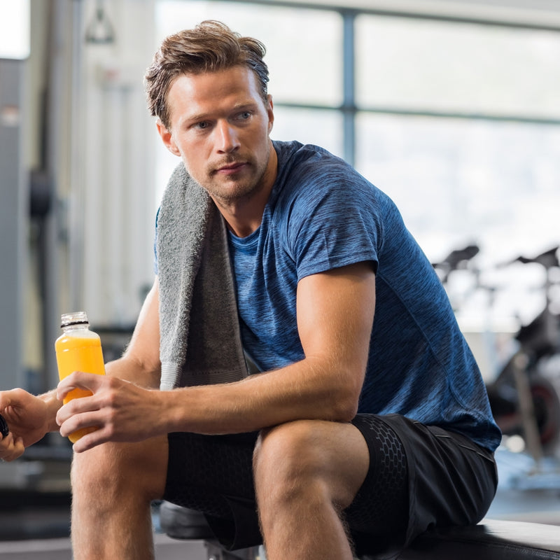 Man in a gym holding an orange drink and towel